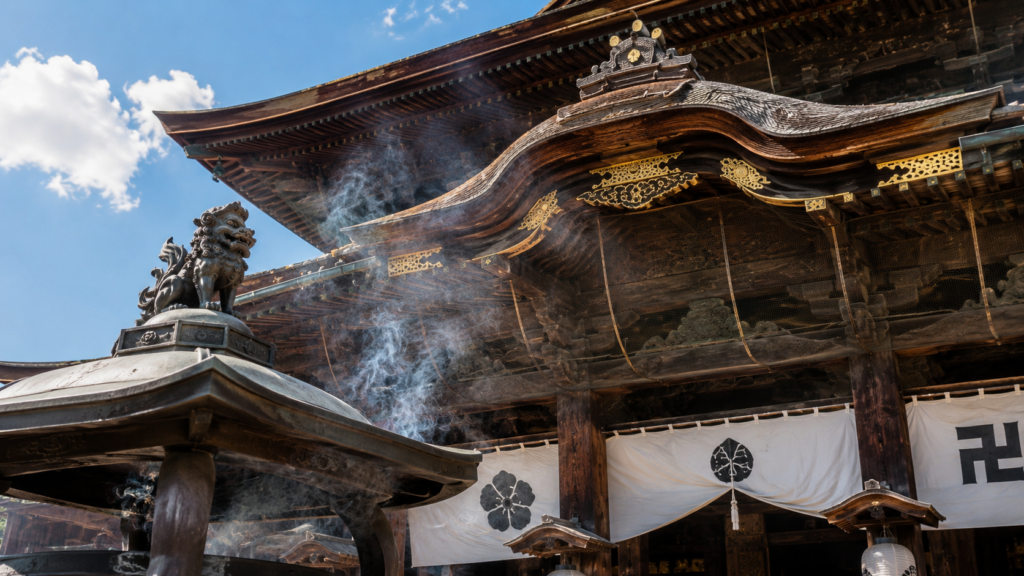 善光寺の歴史ある木造建築と、参拝者の心身を清める大香炉（常香炉）の白い煙